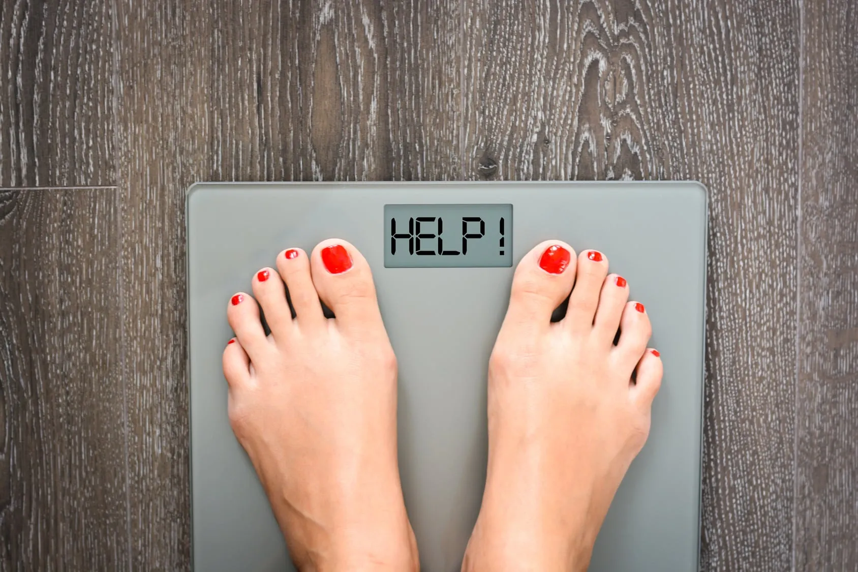 Bare feet on a bathroom scale that reads HELP!
