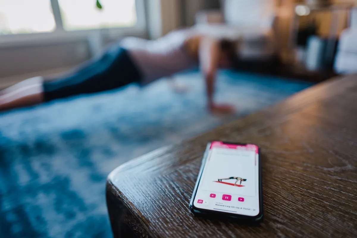 A phone showing a workout video while someone does a plank on a rug behind it